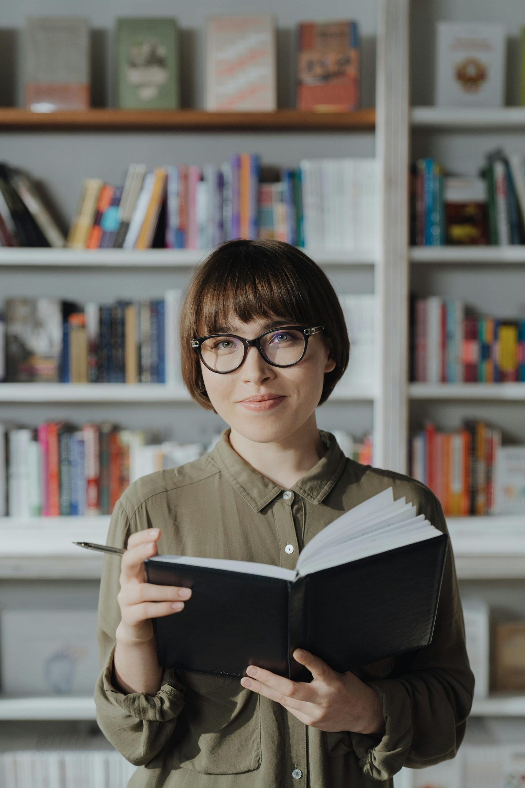femme brune à lunettes qui explique comment réussir en auto-édition devant une bibliothèque