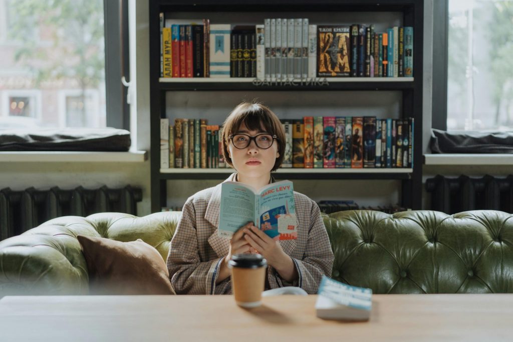 chroniqueuse à lunettes qui lit un livre devant sa bibliothèque