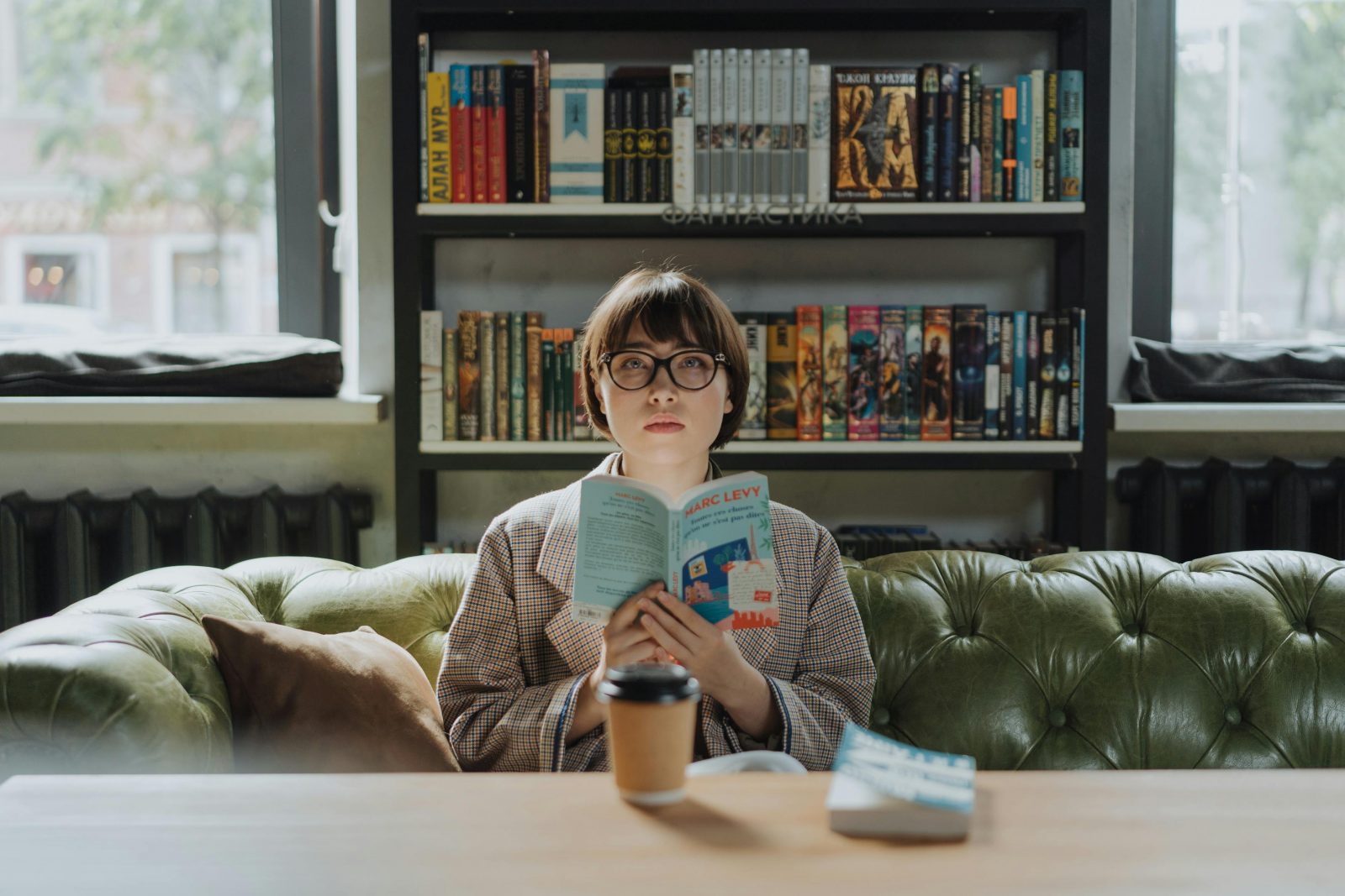chroniqueuse à lunettes qui lit un livre devant sa bibliothèque