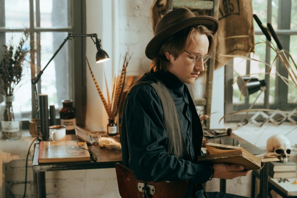 homme amateur de littérature avec un chapeau qui lit un livre sur la mort dans un atelier d'artiste avec un crâne et une lampe