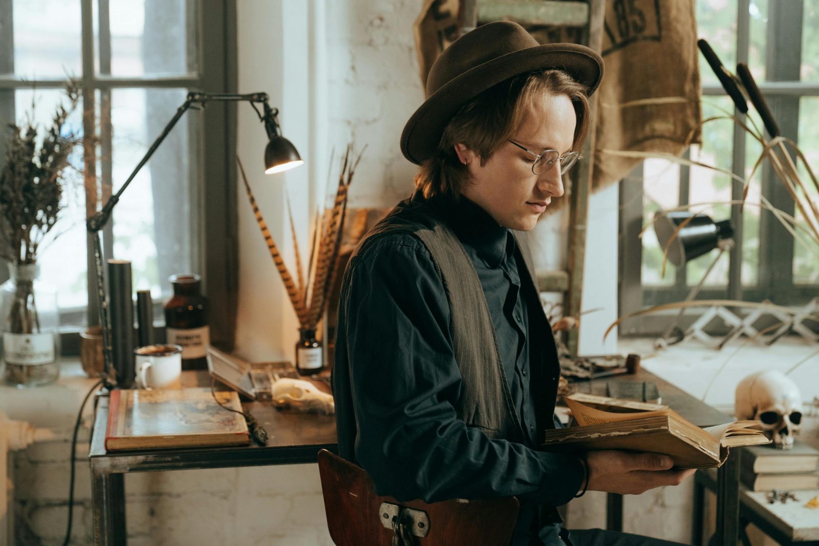 homme amateur de littérature avec un chapeau qui lit un livre sur la mort dans un atelier d'artiste avec un crâne et une lampe